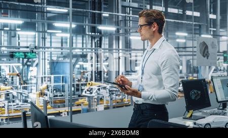 Handsome Engineer in Glasses and White Shirt Using Tablet Computer and Looking Out of the Office at a Car Assembly Plant. Industrial Specialist Working on Vehicle Design in Technological Facility. Stock Photo