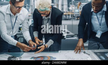 Young Diverse Team of Automotive Engineers Working in Office at Car Factory. Industrial Designer Talks About Electric Engine Parts with Colleagues, Discussing Technical Blueprint for New Vehicle. Stock Photo