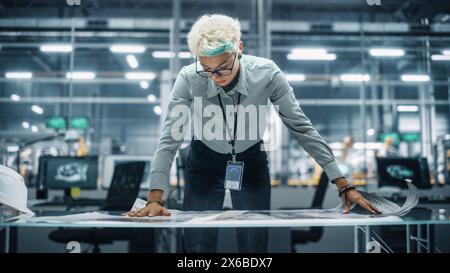 Young Diverse Female Engineer Looking at a Technical Blueprint at Work in an Office at Car Assembly Plant. Industrial Specialist Working on Vehicle Parts in Technological Development Facility. Stock Photo