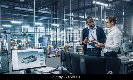 Two Diverse Automotive Industrial Engineers Talking About Vehicle Production while Standing in Office at a Car Assembly Plant. Industrial Specialists Discuss Work Projects on Tablet Computer. Stock Photo