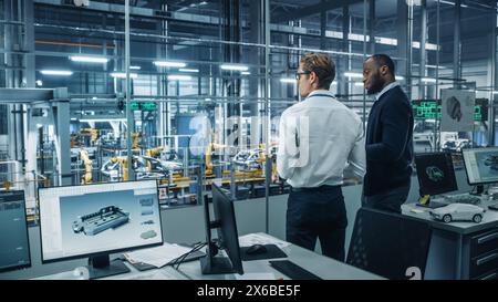 Two Diverse Automotive Industrial Engineers Talking About Vehicle Production while Standing in Office at a Car Assembly Plant. Industrial Specialists Discuss Work Projects on Tablet Computer. Stock Photo