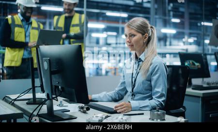 Car Factory: Team of Engineers Discuss Project, Female Technician Working on Computer. Monitoring, Equipment Production. Automated Robot Arm Assembly Line Manufacturing Electric Vehicles. Gliding Shot Stock Photo