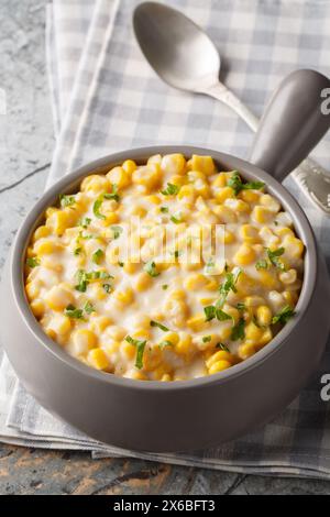 Creamed Corn is a classic side dish consists of tender corn kernels bathed in a rich creamy sauce closeup on the bowl on the table. Vertical Stock Photo