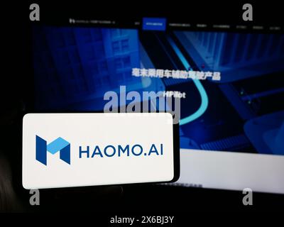 Person holding smartphone with logo of Chinese autonomous driving company Haomo.AI in front of website. Focus on phone display. Stock Photo