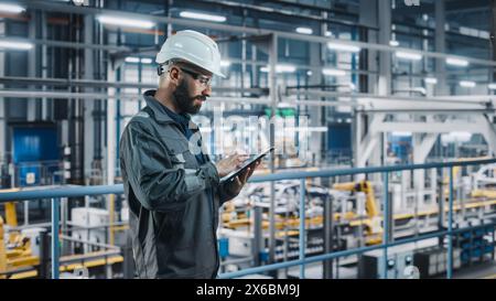 Car Factory Engineer in Work Uniform Using Tablet Computer. Automotive Industry 4.0 Manufacturing Facility Working on Vehicle Production with Robotic Arms Technology. Automated Assembly Plant. Stock Photo