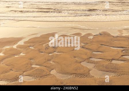 Patterns left in the sand with pools of water after a neap tide on a beach. Waves roll to the the shore. Stock Photo