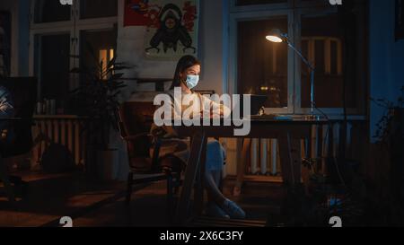 Female Manager in Protective Face Mask Works on Laptop Computer in Creative Agency in Loft Office in the Evening. Renovated Stylish Design with House Plants. Stock Photo