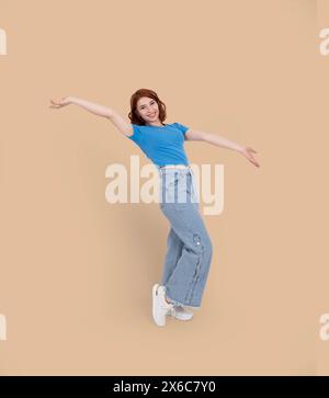 Full length body view young caucasian red short hair teen woman raised arms up. Flying wings. Feel freedom. Happy smiling beautiful teenage posing. Stock Photo