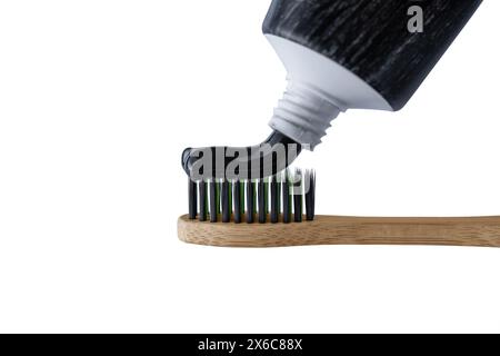 Putting charcoal toothpaste on bamboo toothbrush isolated on white background. Swatch of black charcoal whitening toothpaste on brush for design. Stock Photo