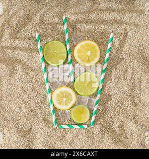 Creative summer composition with lemon and lime slices, drinking straw and ice cubes on sandy background. Minimal drink concept. Top down lemonade. Stock Photo