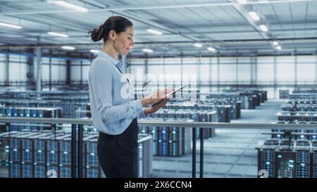 Data Center Engineer Using Tablet Computer. Server Farm Cloud Computing Specialist Facility with Multiethnic Female System Administrator Working with Data Protection Network for Cyber Security. Stock Photo