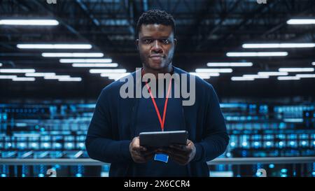 Portrait of a Data Center Engineer Using Laptop Computer. Server Room Specialist Facility with Black Male System Administrator Working with Data Protection Network for Cyber Security. Stock Photo