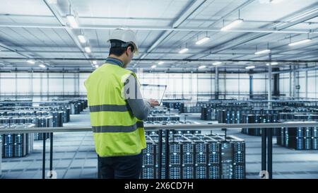 Data Center Engineer in High Visibility Vest Using Laptop Computer. Server Farm Cloud Computing Facility with Asian Male System Administrator Working with Data Protection Network for Cyber Security. Stock Photo