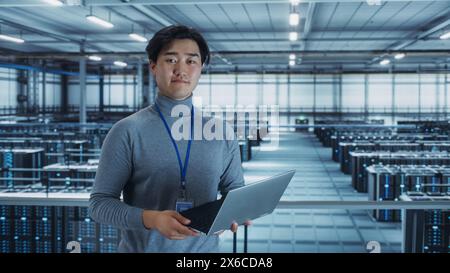 Portrait of a Data Center Engineer Using Laptop Computer. Server Room Specialist Facility with Korean Male System Administrator Working with Data Protection Network for Cyber Security. Stock Photo
