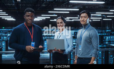 Diverse Team of Data Center System Administrators and IT Specialists Use Laptop and Tablet Computers, Smiling on Camera. IT Engineers work on Cyber Security Protection in Cloud Computing Server Farm. Stock Photo