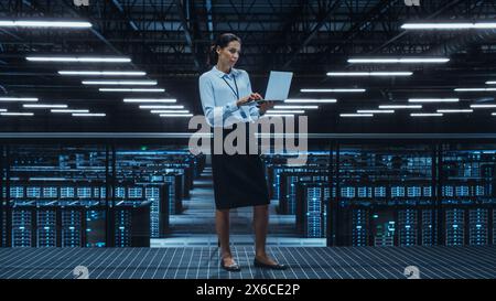 Data Center Engineer Using Laptop Computer. Server Farm Cloud Computing Specialist Facility with Multiethnic Female System Administrator Working with Data Protection Network for Cyber Security. Stock Photo
