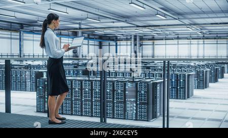 Data Center Engineer Using Laptop Computer. Server Farm Cloud Computing Specialist Facility with Multiethnic Female System Administrator Working with Data Protection Network for Cyber Security. Stock Photo