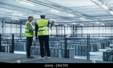 Korean Data Center System Administrators and African American IT Specialists in High Visibility Vests Talk, Use Laptop. IT Engineers work on Cyber Security Network Protection in Server Farm. Stock Photo