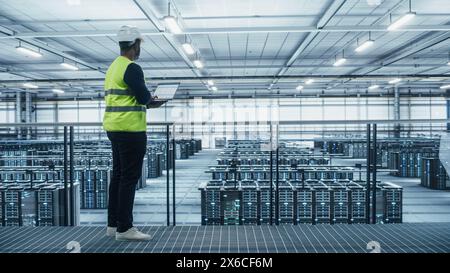 Data Center Engineer in High Visibility Vest Using Laptop Computer. Server Farm Cloud Computing Facility with Black Male System Administrator Working with Data Protection Network for Cyber Security. Stock Photo