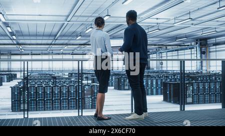 Data Center Female System Administrator and Male IT Specialist Talk, Use Laptop. Information Technology Engineers work on Cyber Security Network Protection in Cloud Computing Server Farm. Stock Photo