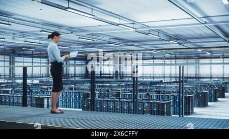 Data Center Engineer Using Laptop Computer. Server Farm Cloud Computing Specialist Facility with Multiethnic Female System Administrator Working with Data Protection Network for Cyber Security. Stock Photo