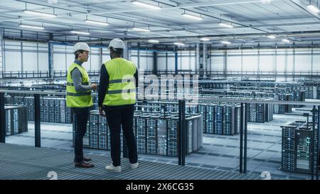 Data Center System Administrators and African American IT Specialists in High Visibility Vests Talk, Use Laptop. IT Engineers work on Cyber Security Network Protection in Server Farm. Stock Photo