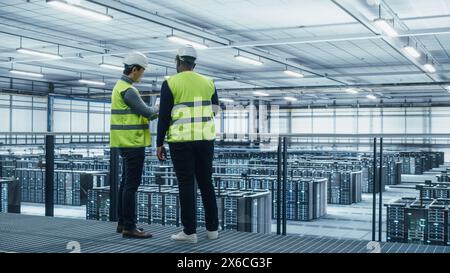 Korean Data Center System Administrators and African American IT Specialists in High Visibility Vests Talk, Use Laptop. IT Engineers work on Cyber Security Network Protection in Server Farm. Stock Photo