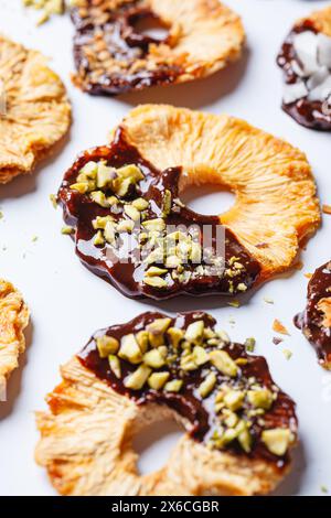 Dried pineapple chips with dark chocolate, pistachio and coconut on a white background. Vegan dessert. Stock Photo