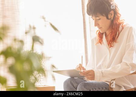 woman using tablet to draw working at home in a quiet space while having a video call red-haired woman smiling Stock Photo