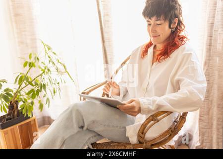 woman using tablet to draw working at home in a quiet space while having a video call red-haired woman smiling Stock Photo
