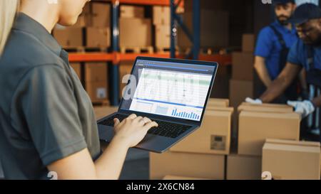 Female Manager Using Laptop Computer To Check Inventory. In the Background Warehouse Retail Center with Cardboard boxes, e-Commerce Online Orders, Food, Medicine, Products Supply. Over the Shoulder Stock Photo