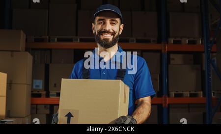 Portrait of Handsome Latin Male Worker Holding Cardboard Box Standing in Warehouse full Goods. Happy Professional Working in Logistics Distribution Center, Delivering e-Commerce Online Orders. Stock Photo