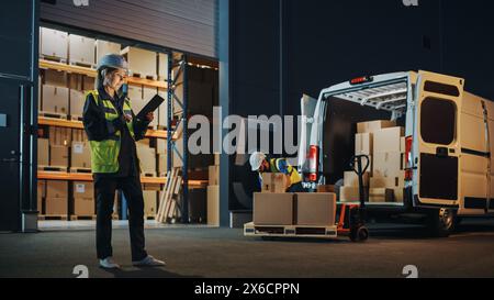 Portrait of Beautiful White Woman Worker Using Tablet Computer in Warehouse full Cardboard Boxes. In Background Professional Loading Cardboard boxes, e-Commerce Online Orders into Truck. Stock Photo