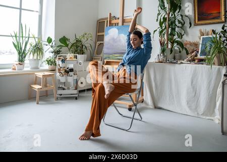 Female artist resting in home creative workspace. Woman enjoys quiet silence taking break from work. Stock Photo