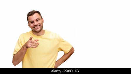 Cheerful man in a yellow t-shirt smiles and points his finger at the camera. Stock Photo
