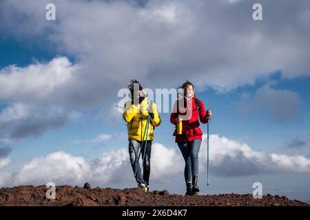 Two hikers on a mountain trail, wearing winter trekking gear, enjoying an outdoor adventure with a cloudy sky background. Stock Photo