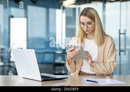 Young businesswoman using a tablet for work in a modern office setting. She is focused and analyzing data Stock Photo