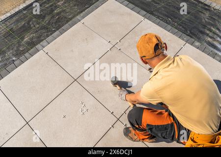 Caucasian worker is installing tiles on a concrete garden patio floor Stock Photo