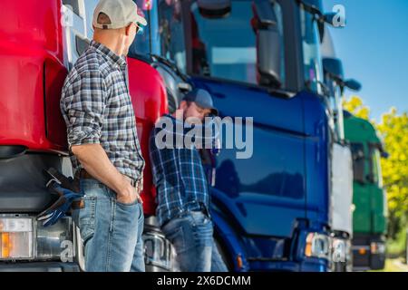 Two truckers standing next to a line of semi trucks in a parking lot. Stock Photo