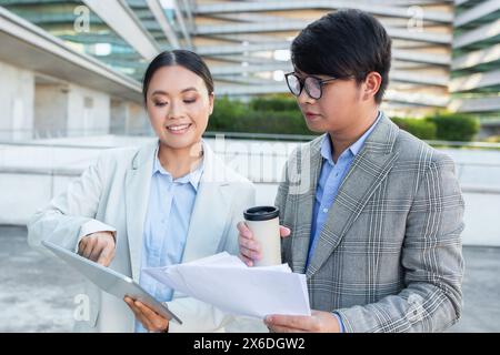 Two Asian Business People Examining Document, Checking Tablet Stock Photo