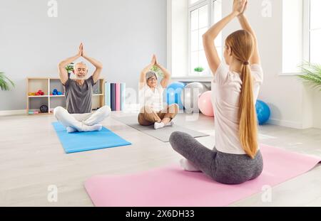 Mature senior people sitting on the floor on mat and practicing yoga in gym in Lotus pose Stock Photo