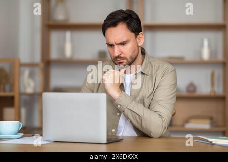 Pensive Man Working on Laptop in a Home Office Setting Stock Photo