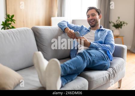 Happy Man Reclining on Couch Using Phone Stock Photo