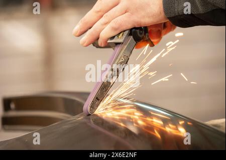Close-up shot captures a skilled worker using an angle grinder to cut through metal, sending bright sparks flying in a workshop. Stock Photo