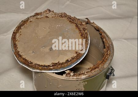 Rusted old metal paint tin with open lid on drop cloth brown expired storage. Stock Photo