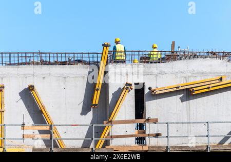 Construction workers collaborating on concrete building structure under clear sky Stock Photo