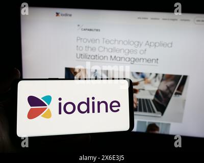 Person holding smartphone with logo of US healthcare AI company Iodine Software LLC in front of website. Focus on phone display. Stock Photo