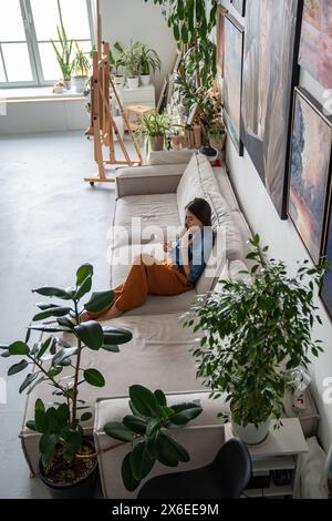 Lazy woman sitting on couch using phone. Girl texting chatting online, spending time on internet. Stock Photo