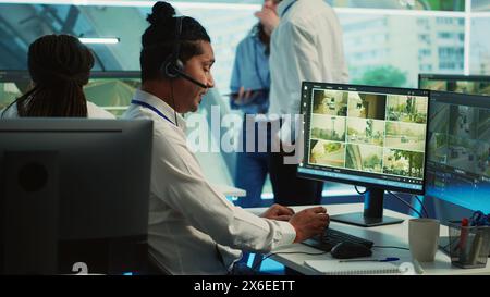 Indian employee communicating satellite map directions in observation room, monitoring traffic around the city via CCTV security system. Young man works with video surveillance data. Camera A. Stock Photo