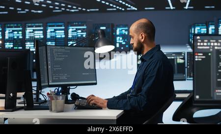 IT engineer programming in server hub housing advanced equipment storing massive datasets. Technician typing code on computer to mend data center racks doing complex computational operations Stock Photo